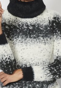 Langärmliger Pullover mit schwarzem Rollkragen und flauschiger Textur. Hat ein verlaufsförmiges Muster in Schwarz, Weiß und Grau. Mit akzentuierten Bündchen.