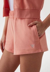 Lichtroze katoenen shorts met een geribde tailleband, voorzien van een zijzak en een zilveren gespijkerde driehoeklogo op de onderste zoom.