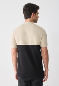 Herre polo skjorte med en beige øvre del og svart nedre del. Korte ermer, krage-design og en teksturert overflate.