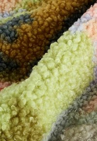 Gros plan d’un tissu texturé et bouclé avec des rayures douces multicolores en jaune, marron, gris et tons pastels.