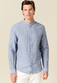 Camicia a maniche lunghe blu chiaro con colletto a girocollo, caratterizzata da un sottile motivo a righe verticali e chiusura con bottoni frontale. Tessuto dalla superficie liscia.