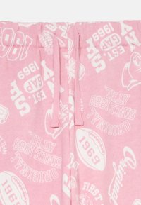 Calças de sudoeste cor-de-rosa com um padrão repetido de logótipos e números em branco, com um cordão na cintura e um tecido suave e texturizado.