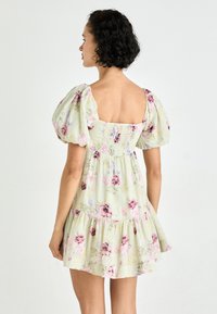 Blommig klänning i ljusgrön tyg med puffärmar, fyrkantig rygg och lager av volanger i fållen. Har mönster i rosa och mörk ros.