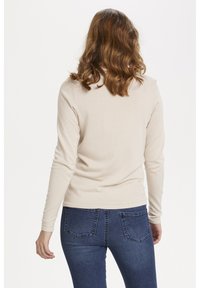 Beige långärmad topp med figurnära design och rund halsringning. Kombinerad med mörkblå jeans med bakfickor och lätt stretch.