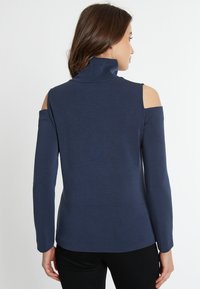 Marineblaue Langarmbluse mit Stehkragen und Kalt-Schulter-Design. Glatte, leicht strukturierte Stoffqualität. Taillierte Silhouette, schlichter Stil.