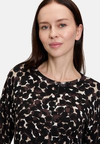  kardigan w zwierzęcy wzór w odcieniach czerni, brązu i kremu. Posiada okrągły dekolt oraz guziki z przodu. Teksturowany materiał.