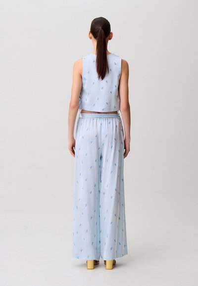 Top corto azzurro chiaro e pantaloni a gamba larga abbinati con piccoli motivi floreali. Tessuto liscio con vita elasticizzata. Scarpe con tacco largo.