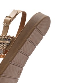 Tan sandal featuring a textured rubber sole, thin adjustable strap with a gold buckle, and woven details across the front.