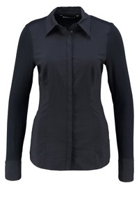 Chemise noire à manches longues en tissu lisse, avec un col boutonné, une patte de boutonnage à l'avant et des détails contrastants aux poignets.