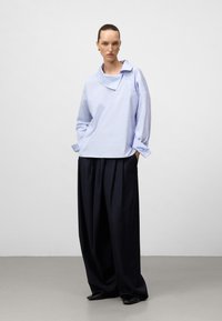 Jasnoniebieska, oversize koszula z szerokim kołnierzem i trzema guzikami, w zestawieniu z ciemnymi, szerokimi spodniami. Gładki materiał i dopasowany krój.