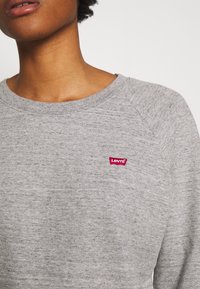 Felpa grigia con scollo rotondo e maniche raglan, realizzata in tessuto texturizzato. Presenta un piccolo logo rosso di Levi's sul petto.