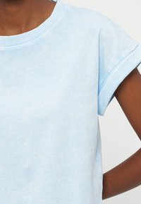 Κοντινό πλάνο ενός ατόμου που φοράει ανοιχτό μπλε κοντομάνικο μπλουζάκι με λεπτομέρεια ρεβέρ στο μανίκι.