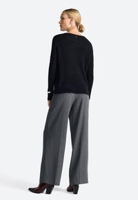 Schwarzer strukturierten Pullover mit lockerer Passform, kombiniert mit grauen, weit geschnittenen Hosen und dunklen, hochhackigen Schuhen. Einfaches Design mit minimalen Details.