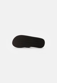 Semelle de chaussure en caoutchouc noir avec un motif de tread en zigzag, bords arrondis et surface texturée pour l'adhérence. Design plat, sans marque visible.