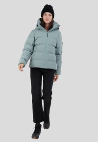 Chaqueta de abrigo azul claro con cremallera frontal, capucha y detalles en negro, combinada con pantalones negros y botas negras. Textura suave y diseño acolchado.