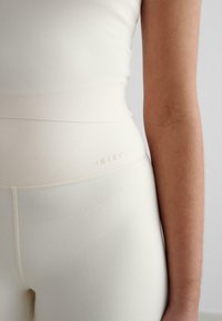 Top aderente color crema e leggings a vita alta realizzati in tessuto morbido ed elasticizzato. Presenta un logo discreto e cuciture lisce.