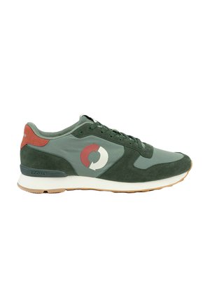 Zapatilla verde y gris con suela de goma y detalle rojo en el talón, con un logotipo circular rojo y blanco en el lateral y marca ecológica en el talón.