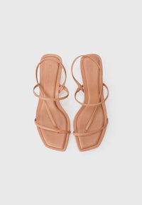 Par med brune strappy flate sandaler med firkantet tå og tynne stropper, lagt side om side på en hvit bakgrunn.