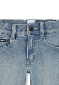 Jasnoniebieskie dżinsy z lekko wyblakłą teksturą, z czarnym zapięciem na guzik, strefowanymi akcentami oraz metką z logo na pasie.