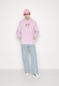 Rozā kapuce ar auklu, kas rotāta ar krāsainu grafiku uz priekšpuses. Vērts ar gaiši zilām platām biksēm un baltiem sporta apaviem.