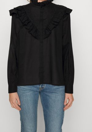 Schwarze Bluse mit Rüschenausschnitt und bestickten Details. Hergestellt aus einem glatten Stoff, hat sie lange Ärmel und einen Knopfverschluss.