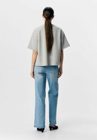 Grijze top met korte mouwen, cropped ontwerp, gecombineerd met lichtblauwe wijde jeans. Model draagt zwarte hoge hakken, met lang stijl haar.