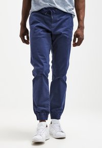 Námořnické modré tepláky vyrobené z jemné bavlny, s elastickým páskem a manžetami, doplněné o bílé tenisky.