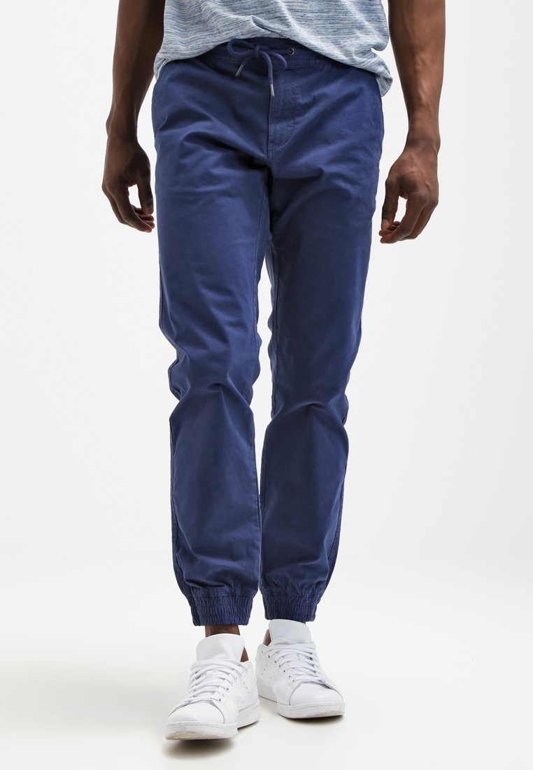 Námořnické modré tepláky vyrobené z jemné bavlny, s elastickým páskem a manžetami, doplněné o bílé tenisky.