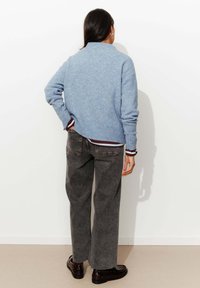 Pull en tricot bleu clair avec un col montant, associé à un jean large gris foncé et des chaussures noires, avec un ourlet et des poignets côtelés.