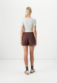 Grå tætsiddende t-shirt parret med brune shorts med elastisk talje. Shortsene har en afslappet pasform. Modellen bærer grå sokker og casual sko.