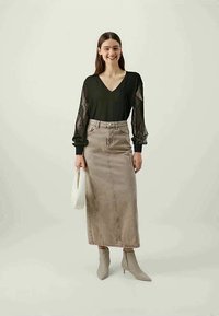 Svart topp med gjennomsiktige blondermerker og V-hals, kombinert med et beige denimskjørt. Grå ankelstøvler og en hvit håndveske fullfører antrekket.