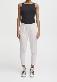 Top de tirantes negro acanalado combinado con pantalones blancos a rayas con líneas rosas y verdes, complementado con zapatillas negras de caña alta.
