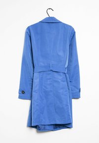 Blå trench coat med långa ärmar, bältesdetalj och knäppta manschetter hängande på en svart galge mot en vit bakgrund.