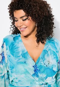 Ljusblå omwrap-klänning med blommönster i nyanser av turkos och vitt, med långa ärmar och djup v-ringning.