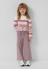 Rosa Pullover mit Rentier- und Zuckerstangenmustern, kombiniert mit weichen, weit geschnittenen lila Hosen. Weiße Sneakers runden das Outfit ab.