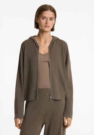 Felpa marrone a costine con zip e cappuccio, caratterizzata da una vestibilità comoda e tasche laterali, indossata sopra un top a scollo a V coordinato.