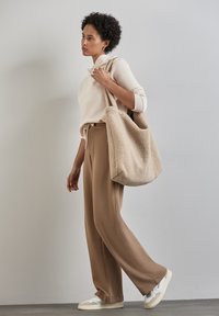 Felpa beige in pile, pantaloni della tuta colorocrema e sneakers bianche. Porta una borsa a tracolla beige e soffice. Texture liscia, vestibilità comoda e design informale.