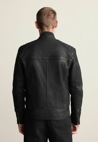 Zwarte leren jas met een getailleerd ontwerp, doorgestikte schouderaccenten en ritssluitingen aan de manchetten. Gladde textuur met minimale stiksels.