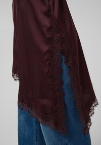 Tissu satin bordeaux foncé avec bordure en dentelle florale festonnée sur un jean en denim bleu sur la partie inférieure du corps d'une personne.