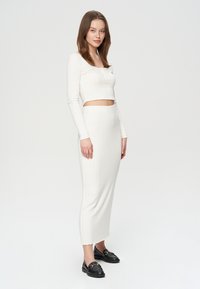 Biały, prążkowany, dzianinowy zestaw składający się z crop topu i długiej spódnicy, z długimi rękawami i dopasowanym krojem, w połączeniu z czarnymi loafersami.