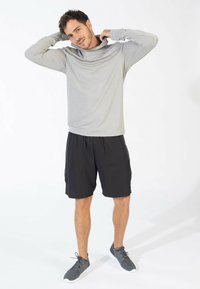 Maglietta grigia chiara a maniche lunghe con scollo ampio, abbinata a pantaloni corti neri. Il modello indossa scarpe sportive grigie. Design semplice e traspirante.