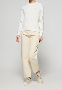 Sweat-shirt blanc avec col rond et ourlet côtelé, associé à un pantalon beige à jambes larges et des baskets beige clair, avec un logo discret.
