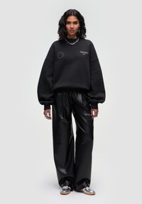 Black oversized sweatshirt with a EU star pattern and logo, paired with glossy black wide-leg pants and shiny silver loafers.