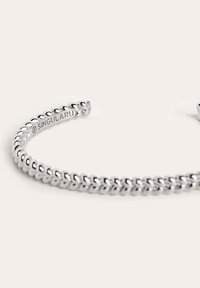 Pulsera de puño de plata con un diseño de eslabones de cadena redondeados y un acabado liso. Marcada con el nombre de la marca "SINGULARU" en su interior.
