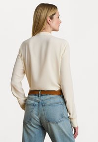 Cream long-sleeve blouse with a smooth texture, paired with light blue high-waisted jeans and a brown leather belt. Simple design with no patterns.
