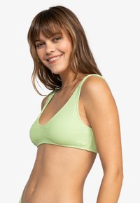 Lys grønn ribbet bikinitopp med brede stropper og dyp V-hals. Teksturert stoff, minimal metallkomponenter og en tettsittende design.
