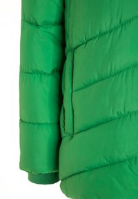 Manche et poche latérale d'une veste matelassée verte avec rembourrage, et bord-côte visible sur fond blanc.