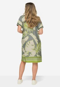 Szara sukienka z krótkim rękawem w dużą zieloną roślinną wzór, z geometrycznym wykończeniem u dołu. Gładki materiał i długość do kolan.