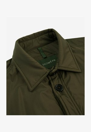 Olijfgroene gewatteerde jas met een puntkraag, zwarte knoopsluitingen en een label met het opschrift "SLOWEAR" zichtbaar bij de hals.