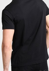 Black cotton t-shirt with short sleeves; features a crew neckline and a relaxed fit. Smooth texture with no visible patterns or accents.